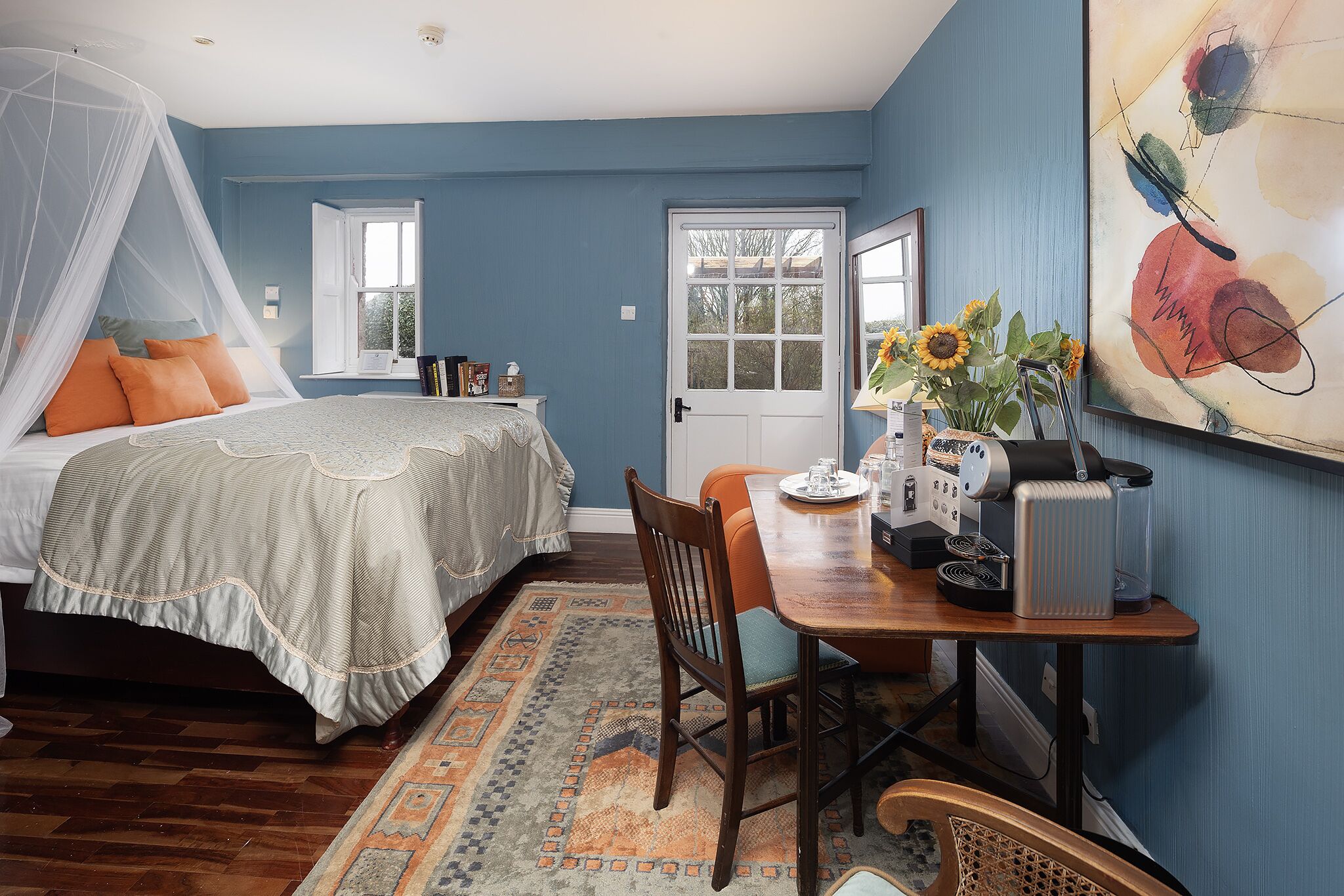 Un dormitorio con una cama, una mesita de noche, un escritorio con una silla, una cafetera y un cuadro en la pared.