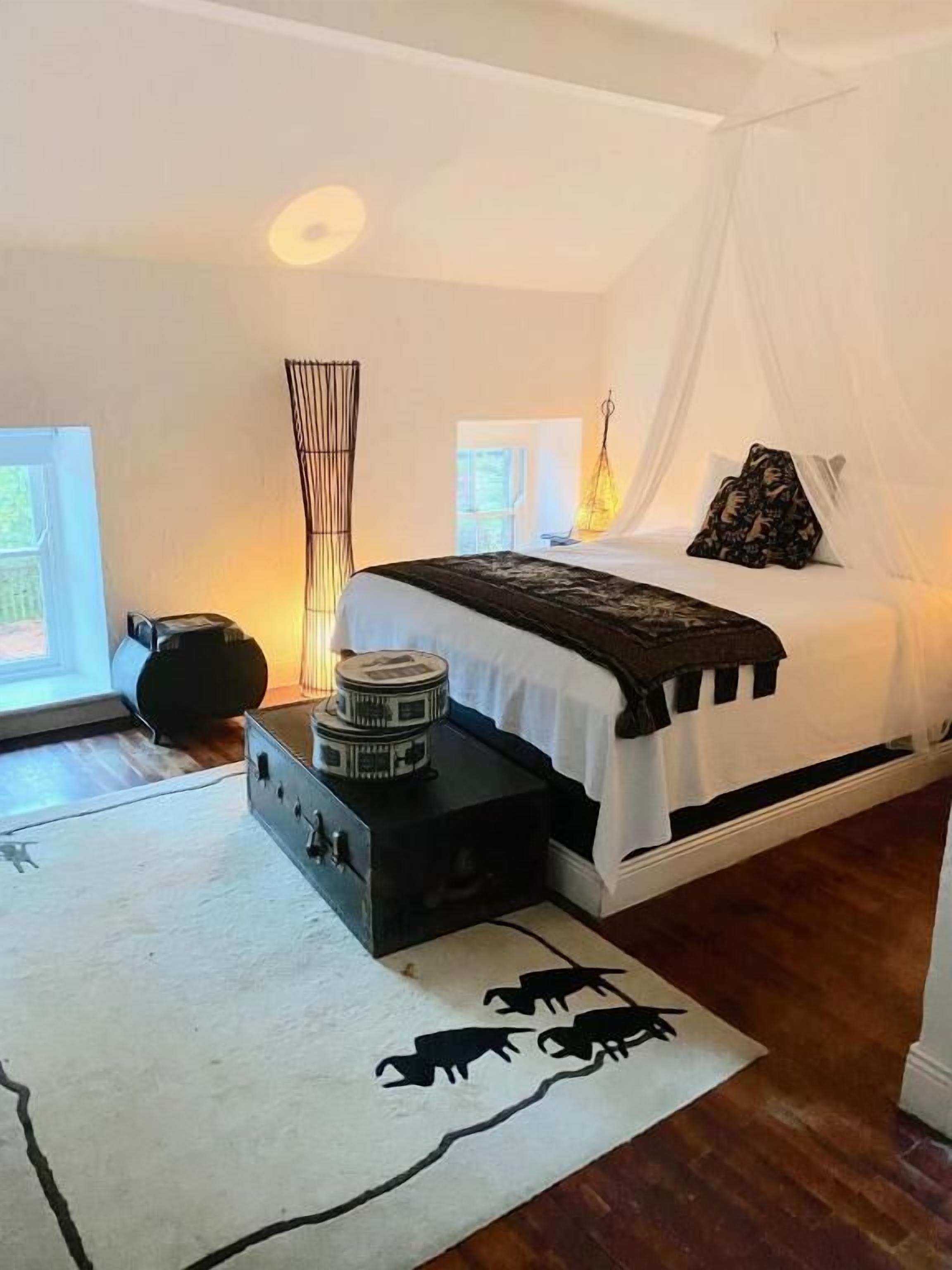 Une chambre à coucher avec un lit, une table de chevet, une lampe et une vue sur l’extérieur.