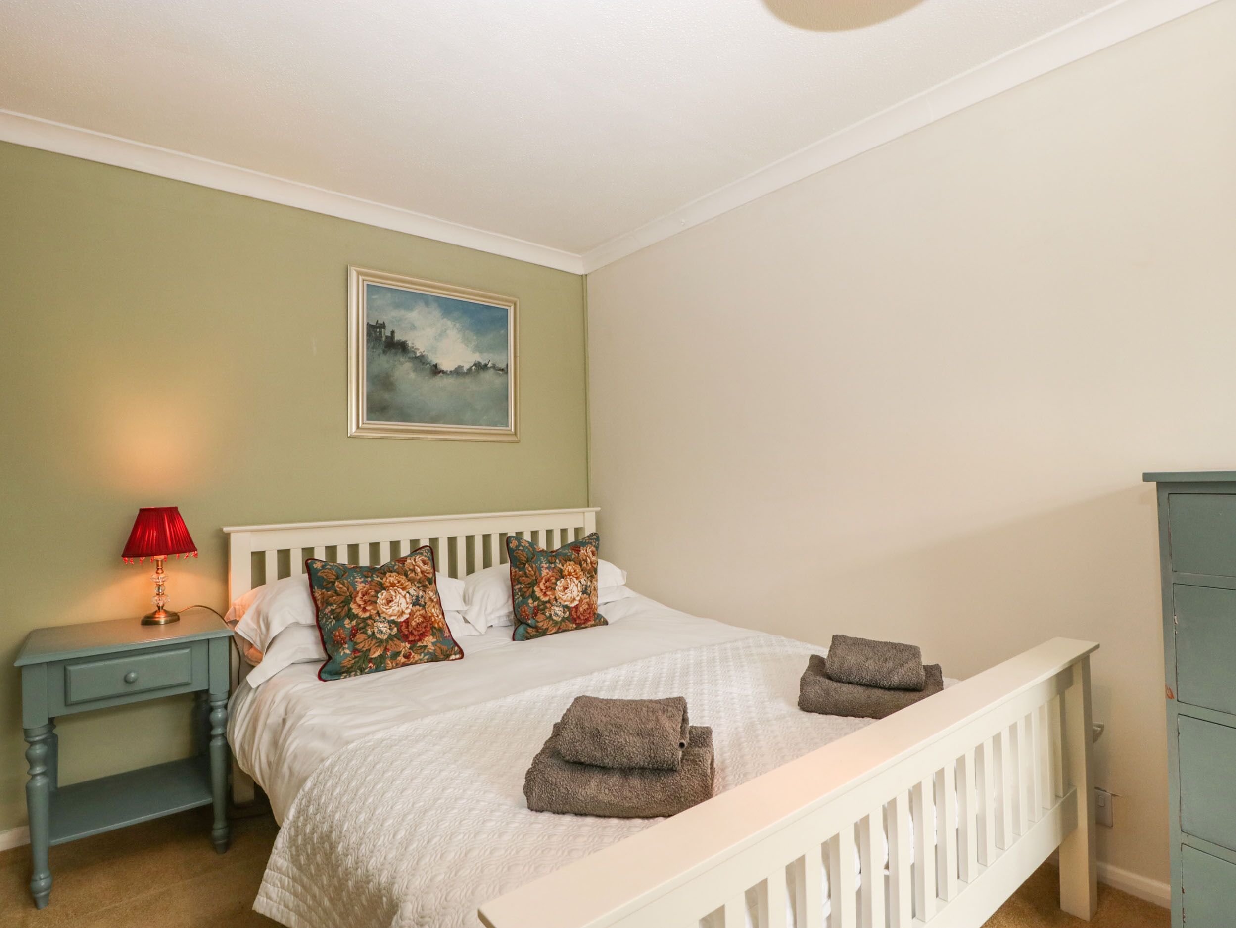 Een slaapkamer met een bed, nachtkastje, lamp, schilderij en een kledingkast.