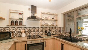 Eine Küche mit Holzausstattung, einem eingebauten Backofen, einer Mikrowelle und einem Spülbecken. Es gibt Regale mit Küchenutensilien und ein Fenster mit Blick.