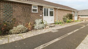 Ein Wohnhaus mit Backsteinfassade, Ziegeldach und einer weißen Tür. Vor dem Haus befindet sich ein kleiner Garten mit verschiedenen Pflanzen und Blumen.