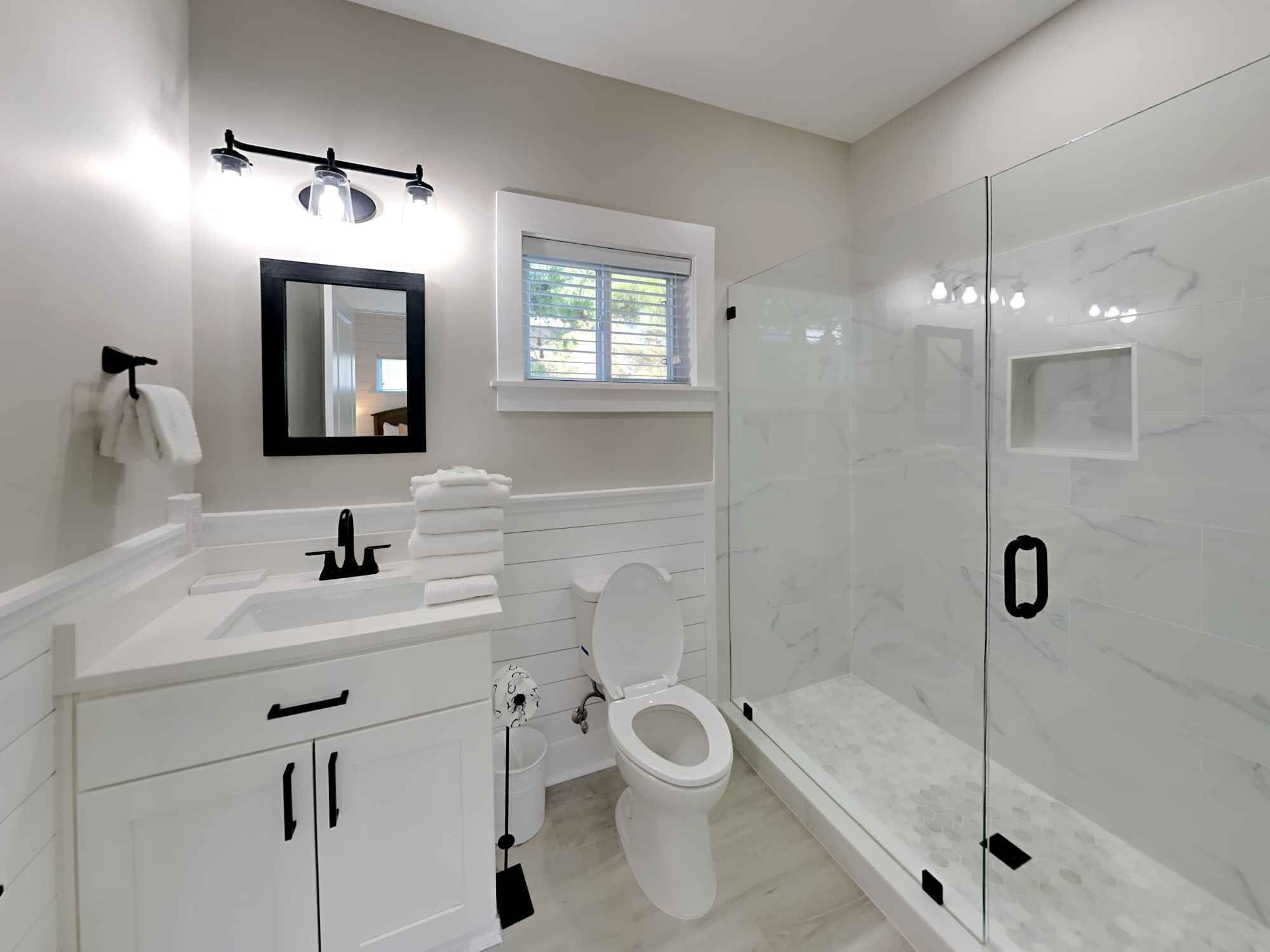 A modern bathroom with a glass-enclosed shower, a white sink with a mirror above it, and a toilet.