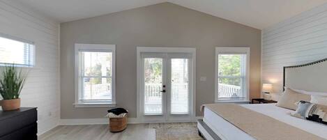 A bedroom with a large bed, two windows, a ceiling fan, and a small side table.