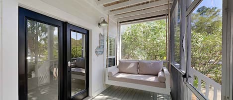 A covered porch with a cushioned seating area, a black door, and a 'hello' mat.