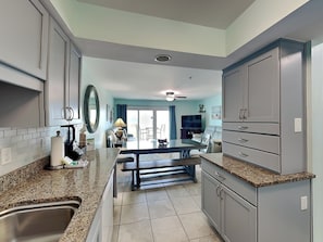 A kitchen with granite countertops, stainless steel sink, and grey cabinetry.