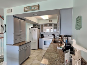 A kitchen with grey cabinets, a white refrigerator, a microwave, and a stove. There is a sign above the refrigerator that reads 'Beach House.' - Dory D | Stunning Location, Easy Beach Access + Pet Friendly (Perdido Key)