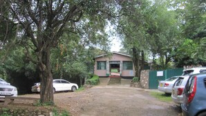 A parking area with a dirt path leading to a building with a green gate. - Sego Safari Lodge (Eldoret)