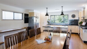 A modern kitchen with a wooden dining table, built-in appliances, and large windows.