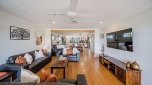 A spacious living room with a black leather sofa, a wooden coffee table, and a TV mounted on the wall.