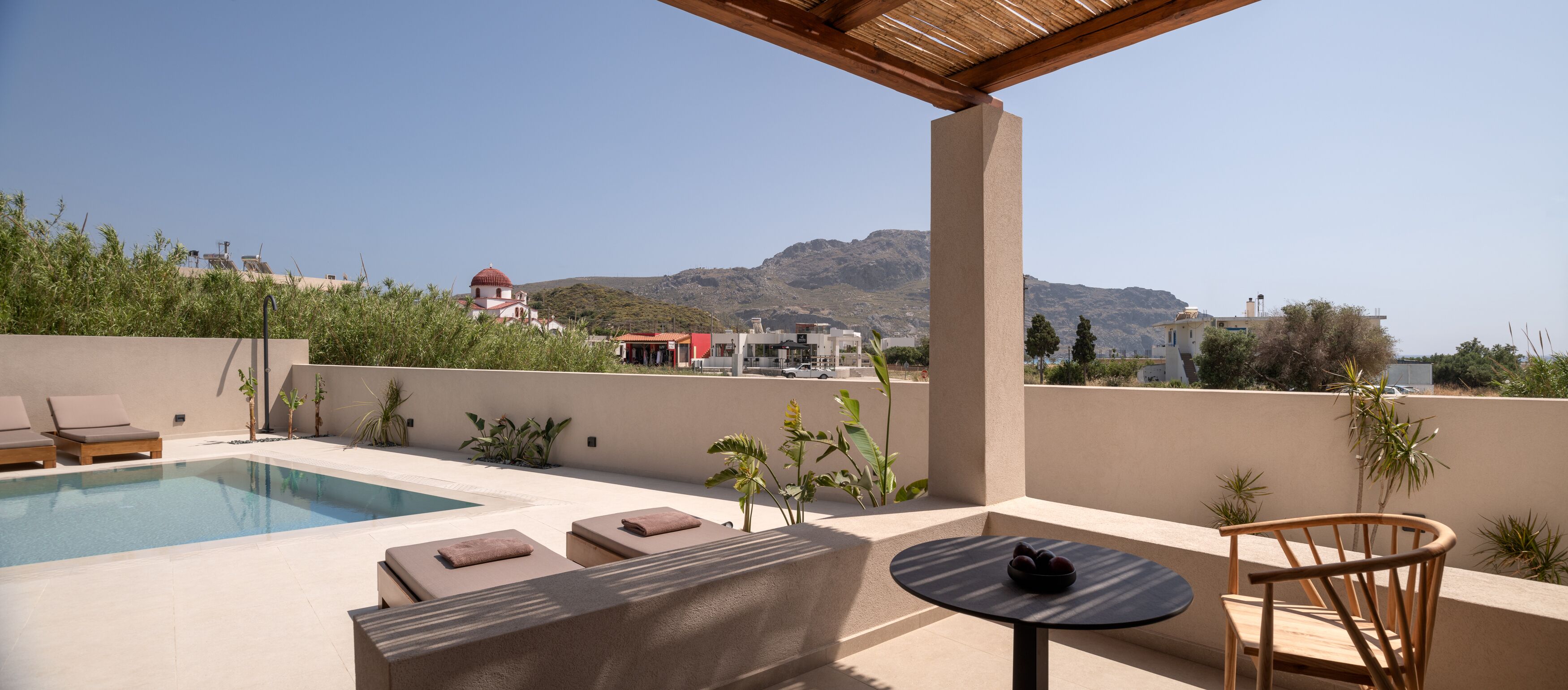 A rooftop pool area with lounge chairs, a table, and a view of a mountain and buildings in the distance.
