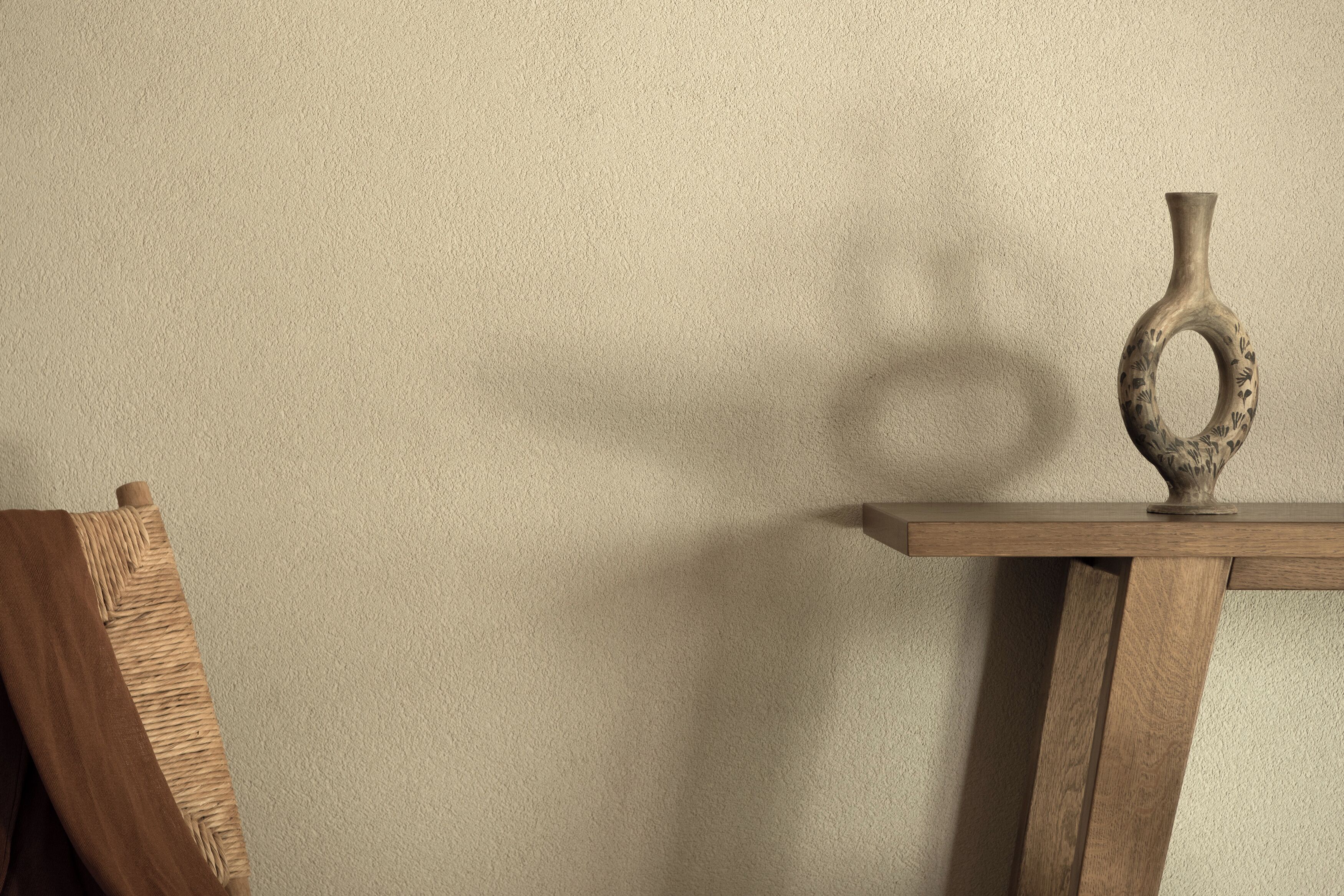 Une table en bois sur laquelle est posé un vase, le tout adossé à un mur à texture.