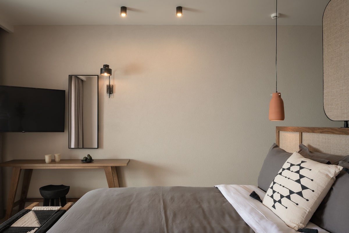 Un dormitorio moderno con cama, mesita de noche y televisor montado en la pared.