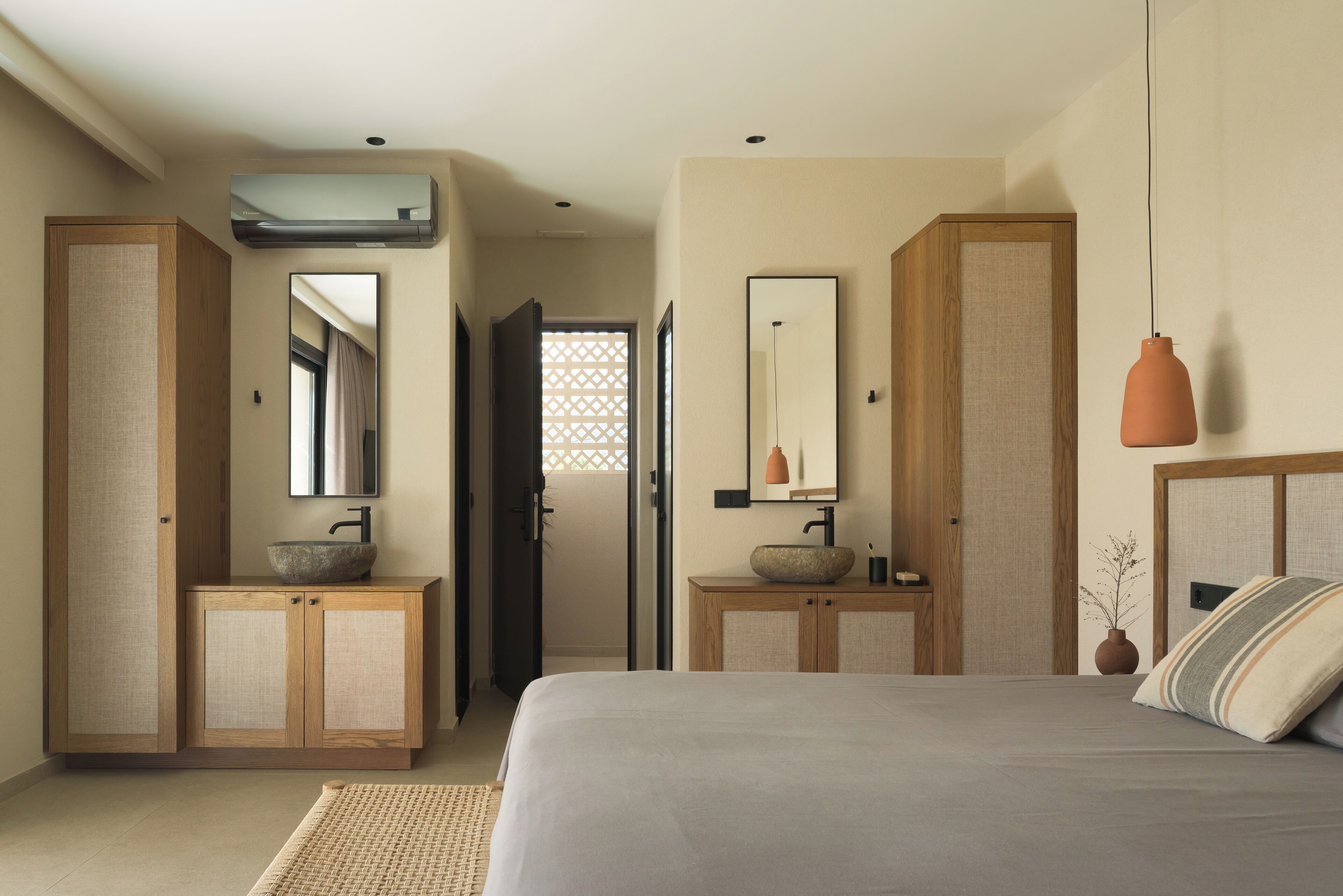 A bedroom with a bed, two wooden cabinets, a mirror, and a hanging pendant light.