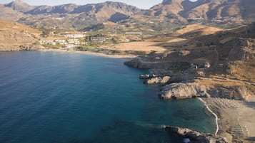 A coastal town with a beach, rocky shoreline, and mountainous backdrop.