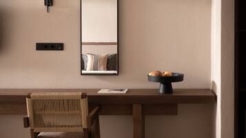 A modern interior with a wooden desk, a woven chair, a black-framed mirror, and a wall-mounted light fixture.