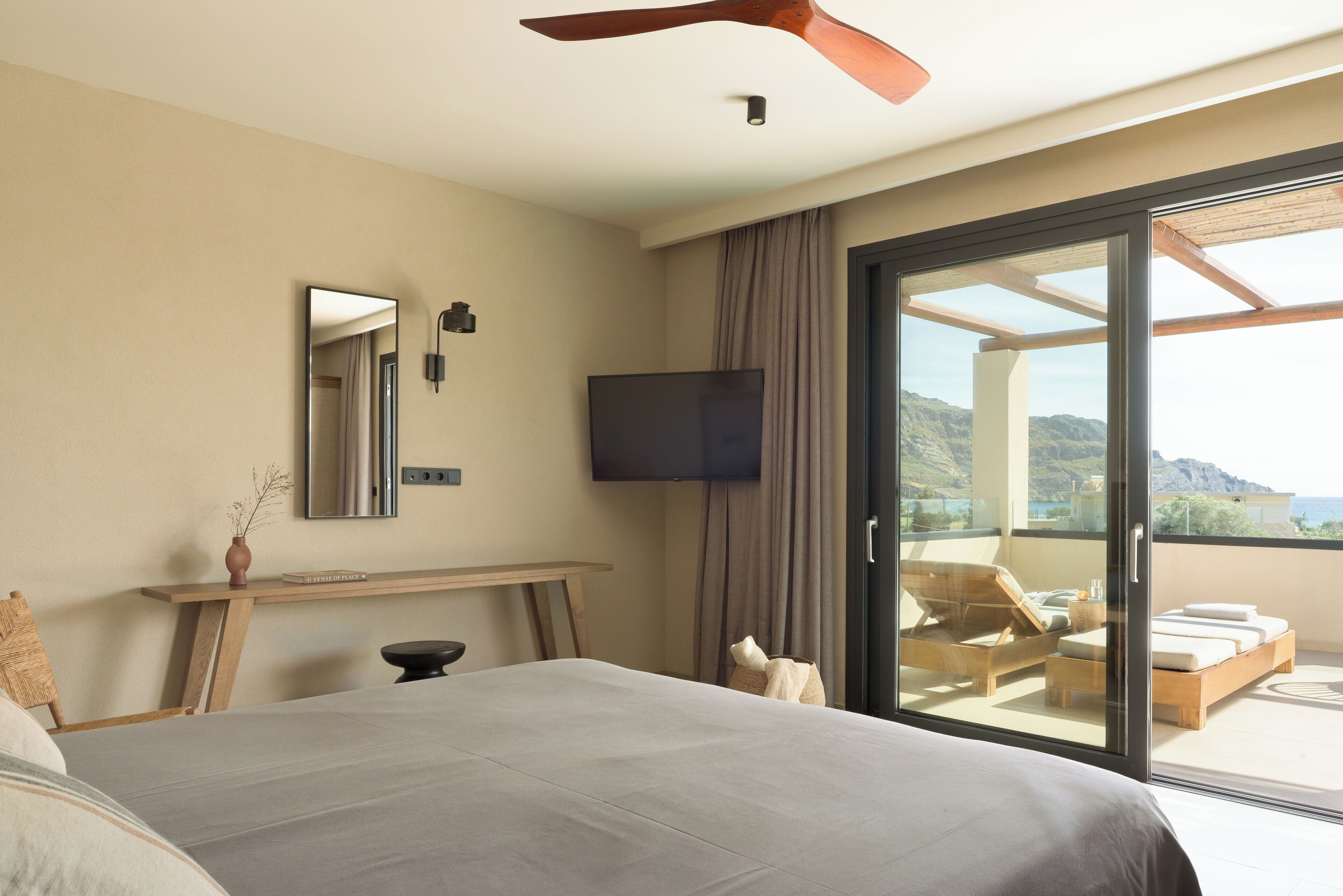 Quarto de hotel moderno com uma cama grande, televisão de tela plana, escrivaninha de madeira e varanda com vista para as montanhas.