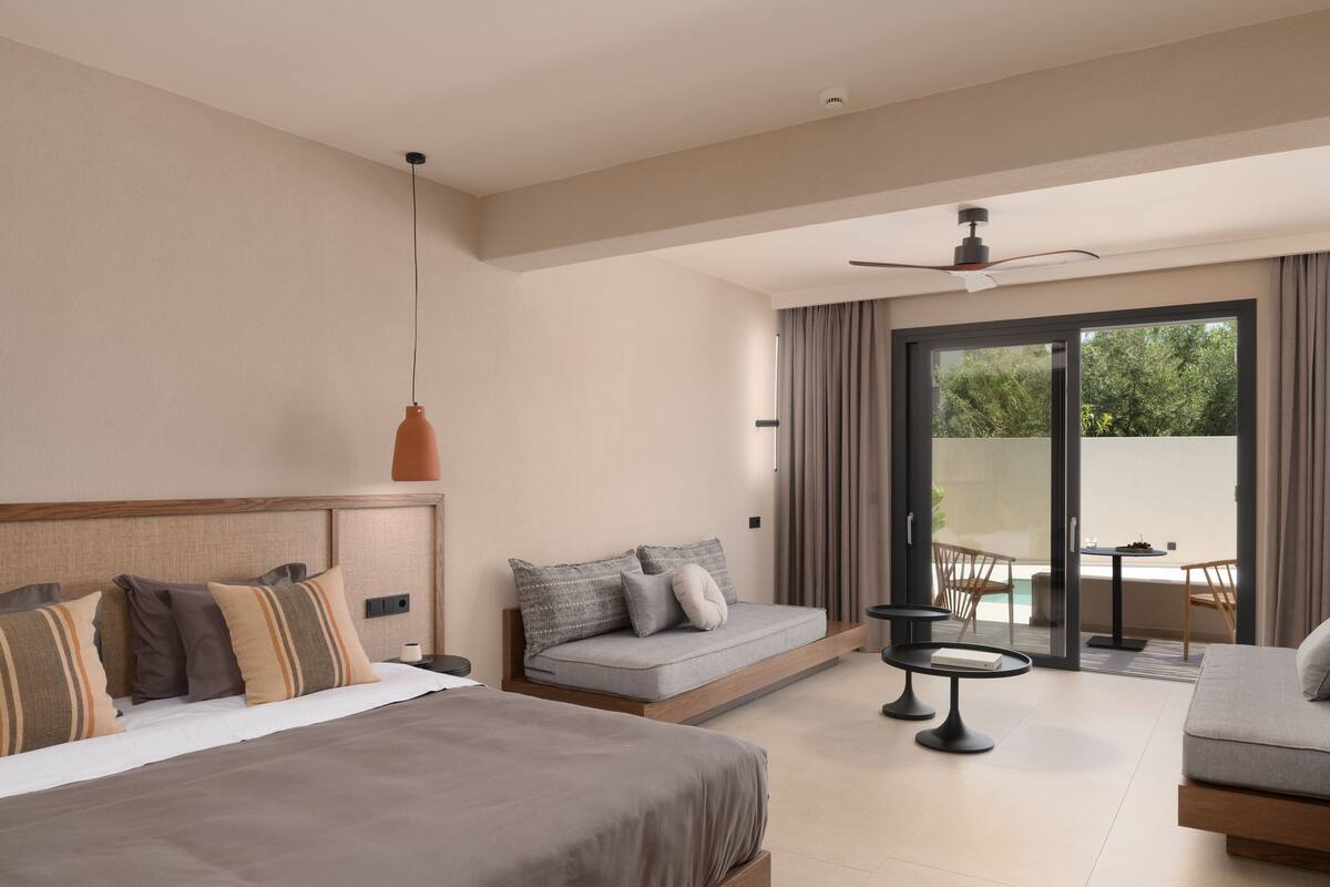 Una habitación de hotel moderna con una cama grande, un sofá, una mesita y un balcón con vistas a zonas verdes.
