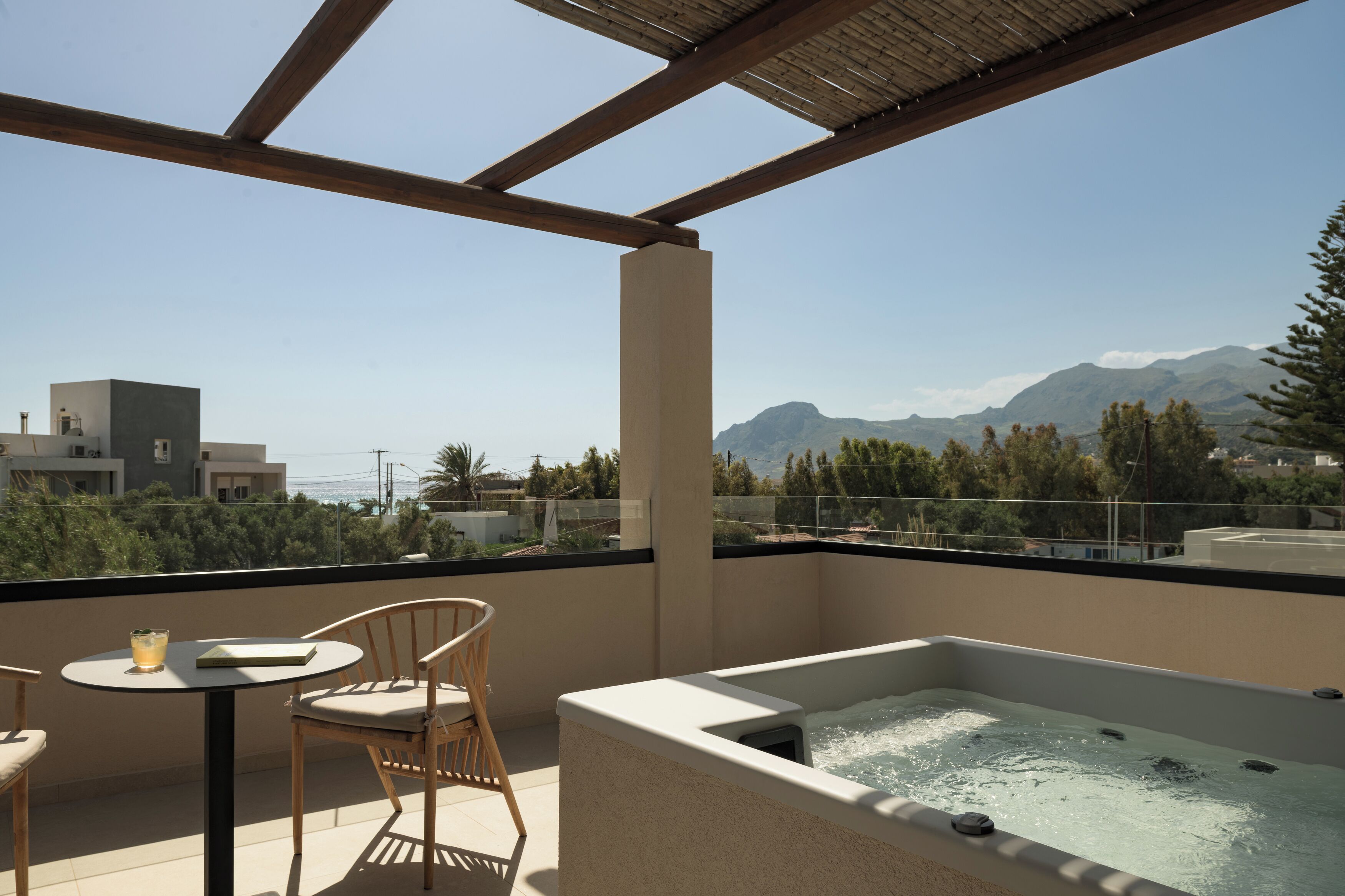 A balcony with a hot tub, a table with chairs, and a view of mountains and buildings.