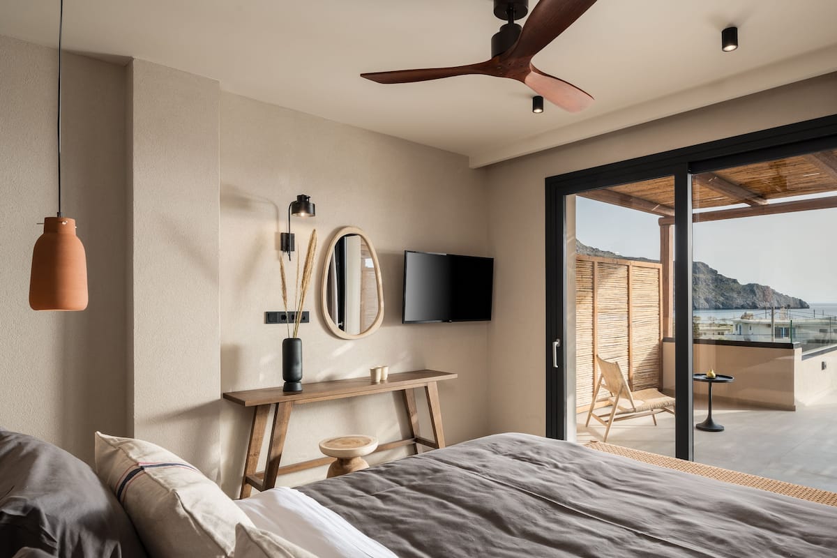 Un dormitorio con cama, televisor, ventilador de techo y vistas al exterior.