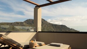 Eine sonnendurchflutete Terrasse mit Liegestühlen und einem Tisch, mit Blick auf eine gebirgige Landschaft.