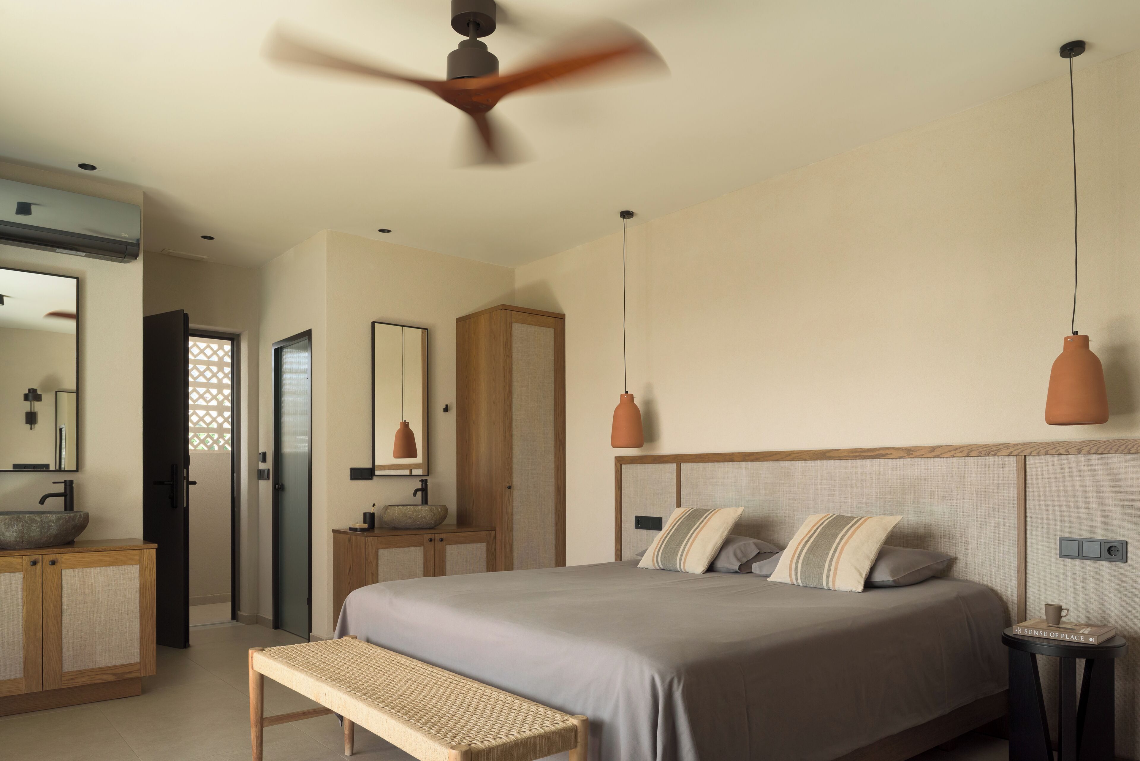 A bedroom with a large bed, bedside tables, a bench, a ceiling fan, and a large mirror.