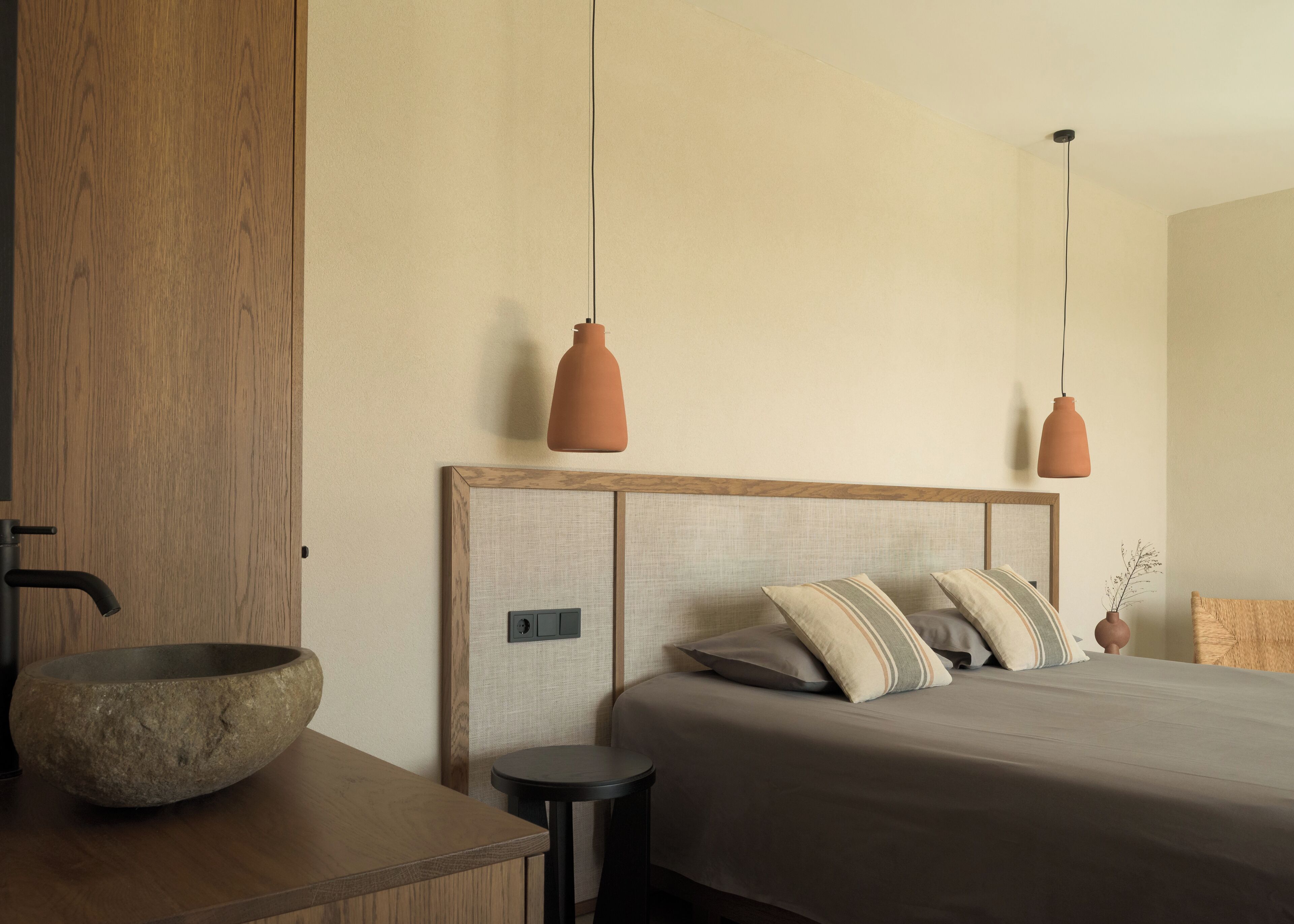 A modern bedroom with a wooden headboard, a large stone bowl on a wooden table, and two pendant lights.