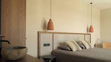 A modern bedroom with a wooden headboard, a large stone bowl on a wooden table, and two pendant lights.