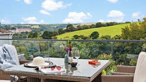 A balcony with a glass table set with a hat, sunglasses, a wine glass, a vase with flowers, and a book. - Spacious Luxury Retreat with parking & views (Kingswear)