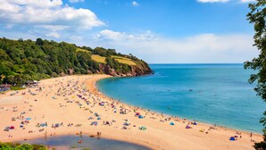 A beach with tents and umbrellas, a sandy shore, and a calm sea. - Spacious Luxury Retreat with parking & views (Kingswear)