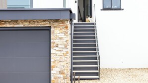A modern house with a stone facade, a grey garage door, and a set of metal stairs leading to a door. - Spacious Luxury Retreat with parking & views (Kingswear)