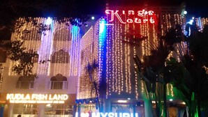 A building with illuminated string lights and neon signs, including "Kudla Fish Land" and "I ♥ Mysuru".
