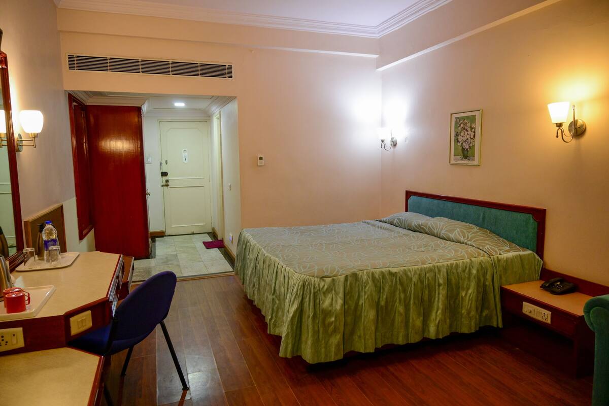 A hotel room with a bed, a desk with a chair, a telephone, and a picture on the wall.