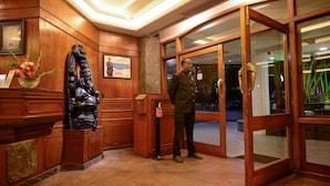 Un área de recepción de madera con una estatua, un certificado enmarcado y un hombre de pie cerca de la entrada.