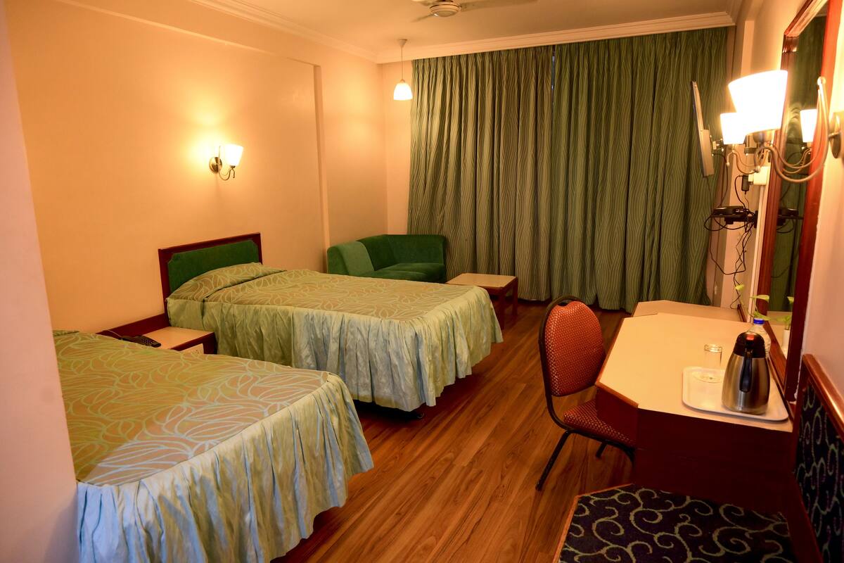 A hotel room with two beds, a desk, a chair, a small table, and a mirror.