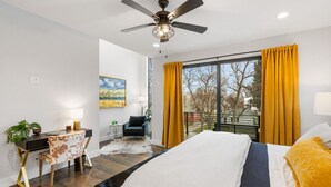 Ein modernes Schlafzimmer mit einem großen Bett, einem Schreibtisch, einem Stuhl und einem Balkon mit gelben Vorhängen.