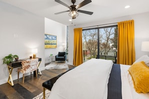 Un dormitorio moderno con una cama grande, un escritorio, una silla y un balcón con cortinas amarillas.