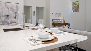 A modern kitchen with a marble countertop, a built-in sink, and a dining area with a white table set for four. - Historic Post Office Loft w/firepit near Zoo (San Diego)