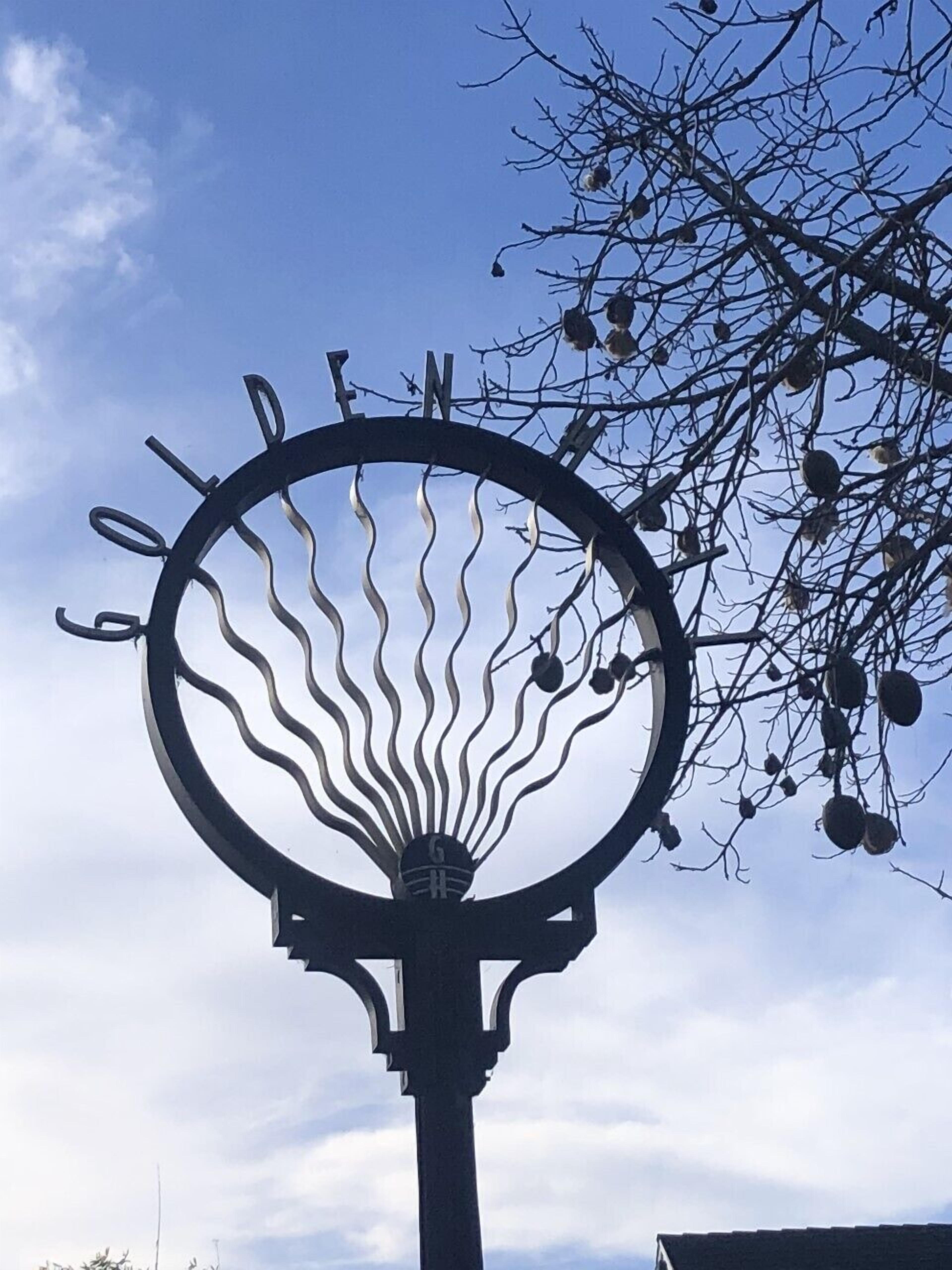 A metal sculpture with a circular design and a tree branch with leaves in the background.