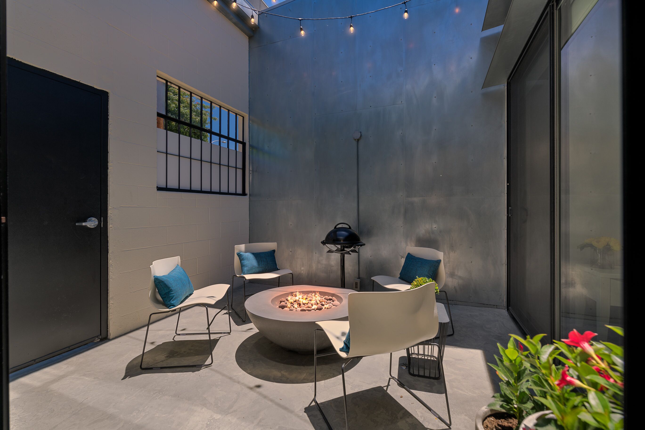 A modern outdoor patio with a circular fire pit, seating, and string lights.