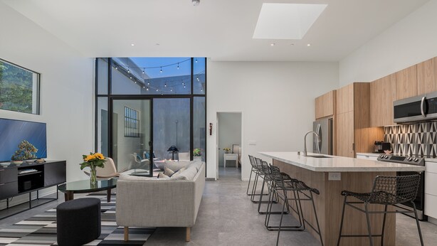 A modern kitchen with a large island, bar stools, and a seating area with a sofa and coffee table. - Historic Post Office Loft w/firepit near Zoo (San Diego)