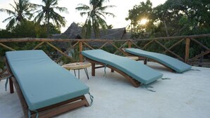 A beachside lounge area with wooden loungers and a small round table. - The Mida Creek (Watamu)