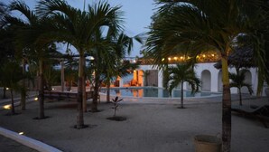 A pool area with palm trees, a building with arches, and a well-lit pool. - The Mida Creek (Watamu)