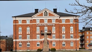 A red-brick building with the name "Carlstad Hostel" on the facade, featuring a central entrance with a small fountain, surrounded by a gravel area. - Carlstad Hostel Sport (Karlstad)