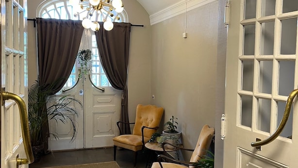 A room with a chandelier, two leather chairs, a potted plant, and a large window with curtains. - Carlstad Hostel Sport (Karlstad)