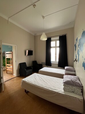 Two single beds with white comforters and pillows, a flat-screen TV, and a cozy armchair.