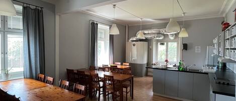 A spacious dining area with wooden tables and chairs, a kitchen with a central island, and pendant lighting.