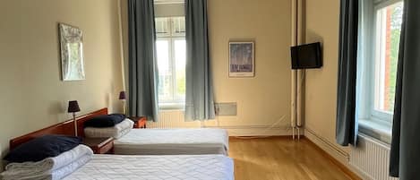 Habitación de hotel con dos camas, piso de madera, televisor de pantalla plana y ventana con cortinas.