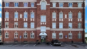 A large, multi-story brick building with a central entrance, multiple windows, and a parking area in front. - Carlstad Hostel Sport (Karlstad)