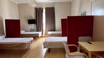 Et hotelværelse med to enkeltsenge, et skrivebord med stol, et fjernsyn og et vindue med gardiner.