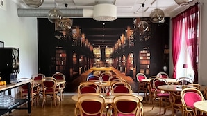 A spacious library with wooden tables and chairs, bookshelves, and hanging pendant lights. - Carlstad Hostel Sport (Karlstad)